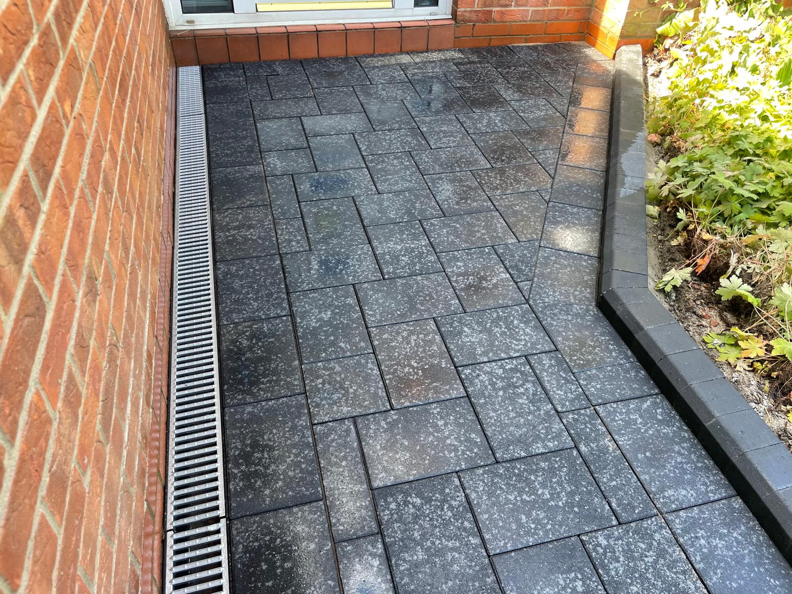 ACO channel drain set flush against the house at the edge of a patio — The Vale Company
