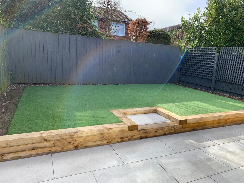 Artificial lawn retained by timber sleepers above a grey porcelain terrace — The Vale Company