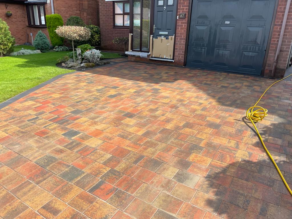 Autumn red tumbled block driveway running up to a garage door — The Vale Company