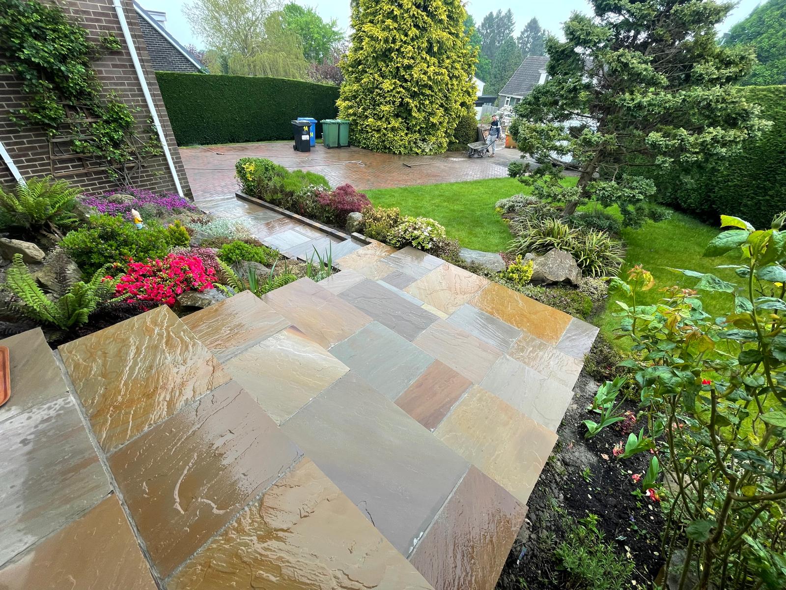 Autumn multi-tone Indian sandstone terrace stepping down past a rockery to a lawn — The Vale Company
