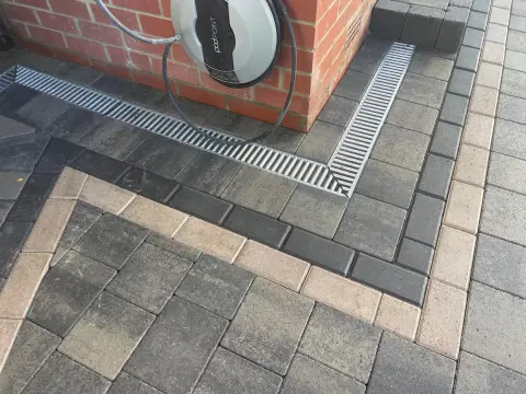 Block paved driveway with channel drainage run past a wall-mounted EV charge point — The Vale Company
