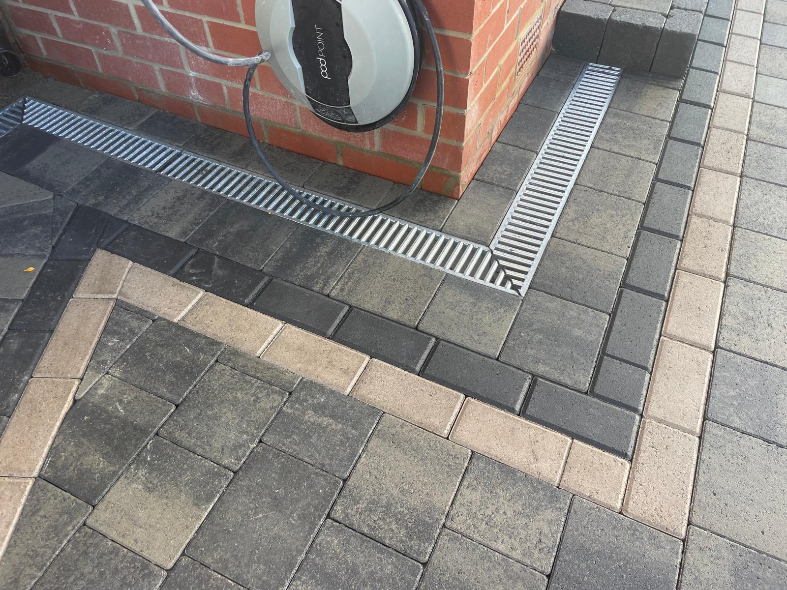 Block paved driveway with channel drainage run past a wall-mounted EV charge point — The Vale Company