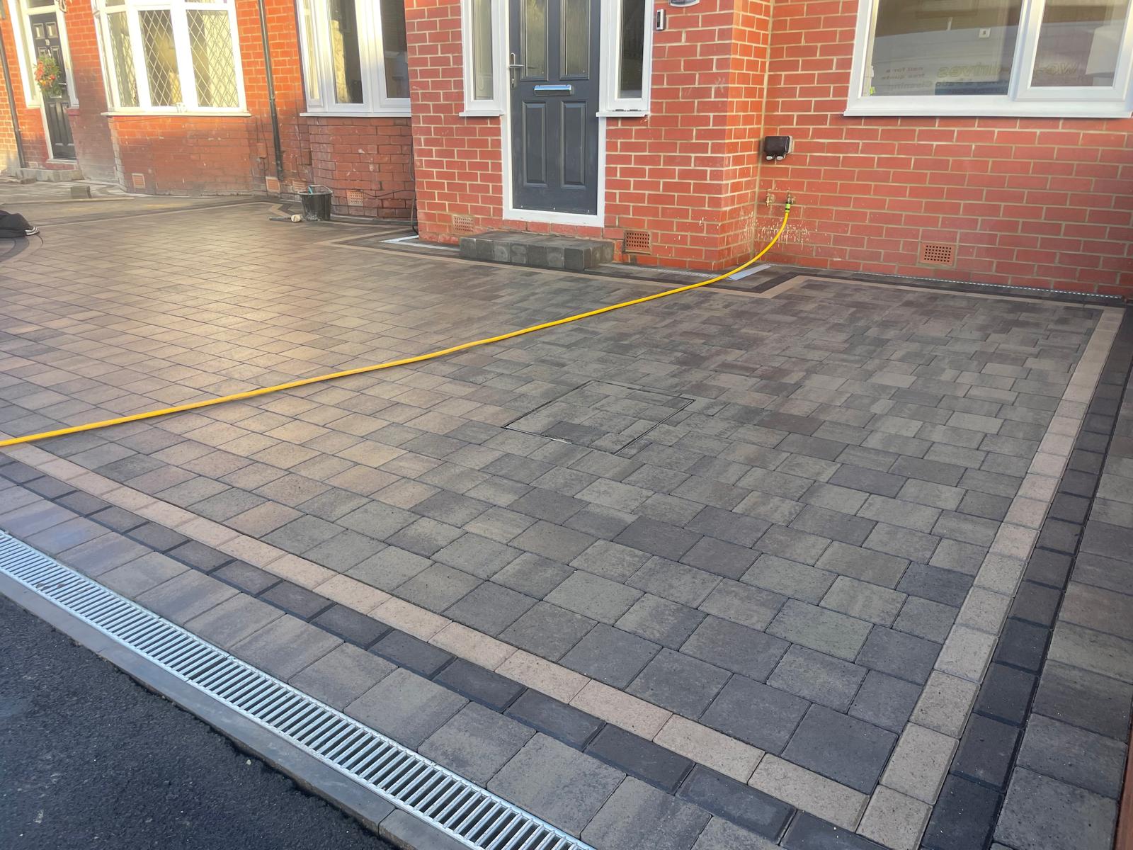 Brindle tumbled block driveway with a charcoal soldier course and channel drain at the road edge — The Vale Company
