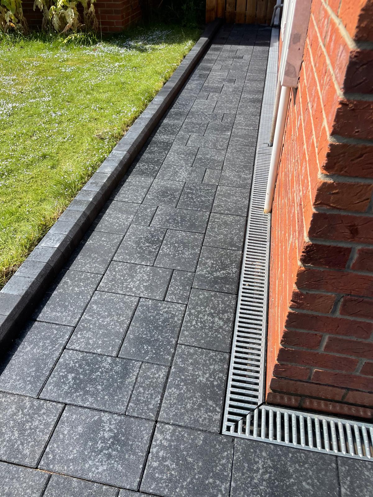 Linear channel drain running flush against a house wall at the edge of the paving — The Vale Company