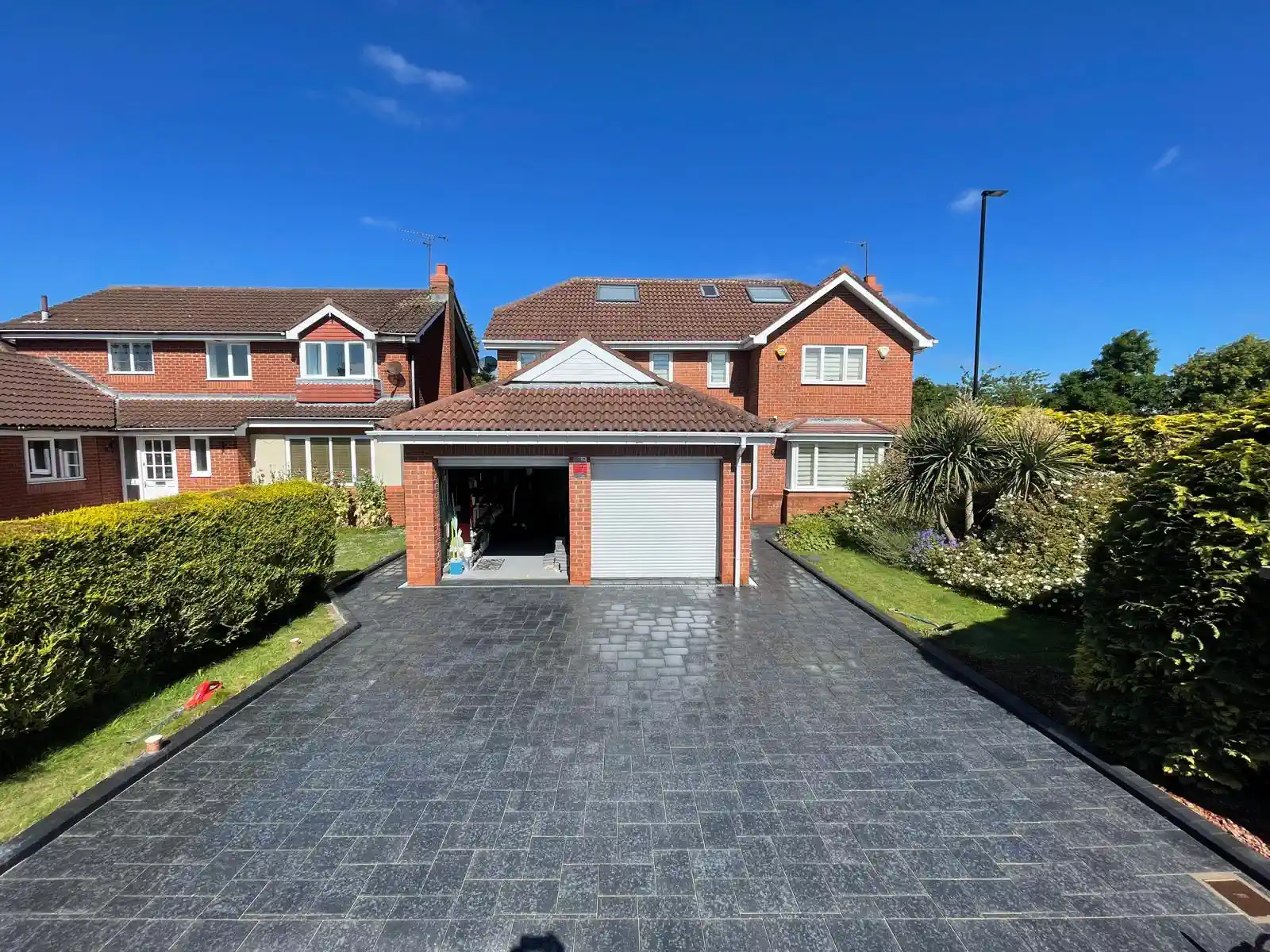 Charcoal tumbled block paved driveway to a double garage, photographed wet — The Vale Company