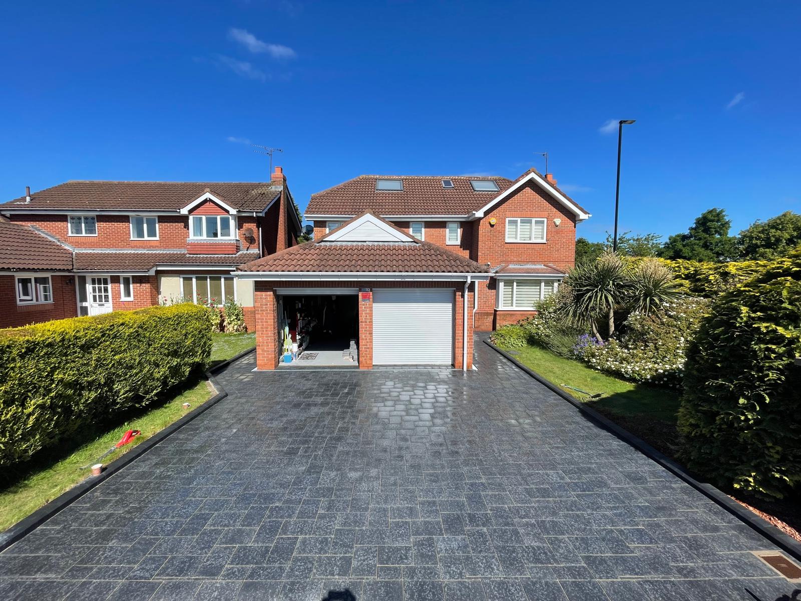 Charcoal tumbled block paved driveway to a double garage, photographed wet — The Vale Company