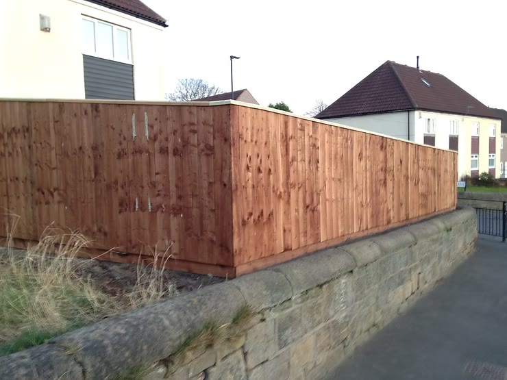 Close-board fence returning a corner above a stone wall, with gravel boards and a capping rail — The Vale Company