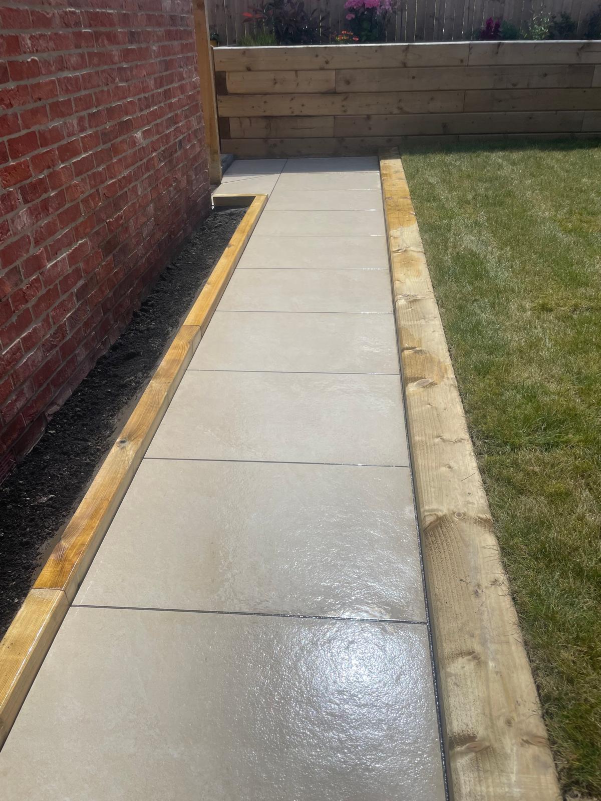 Cream porcelain side path run between timber sleeper edges along a brick wall — The Vale Company