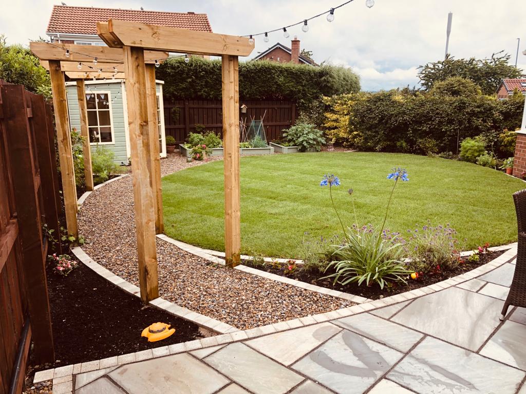 Riven sandstone patio wrapping a lawn with curved brick edging — The Vale Company