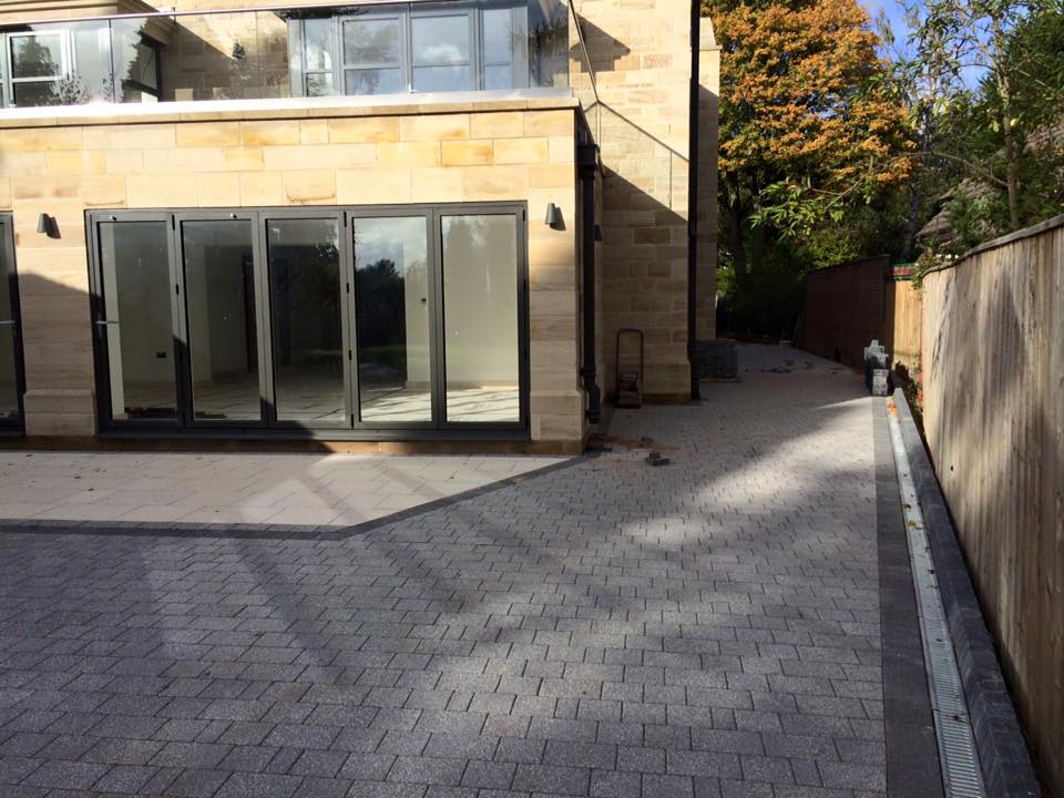 Granite-effect block driveway at a stone-built house with a linear channel drain along the boundary wall — The Vale Company