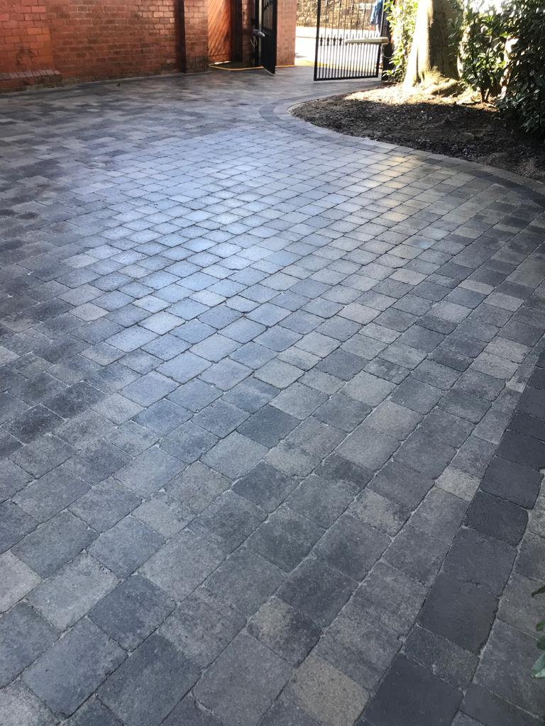 Grey tumbled block driveway with a curved charcoal border sweeping to a gated entrance — The Vale Company