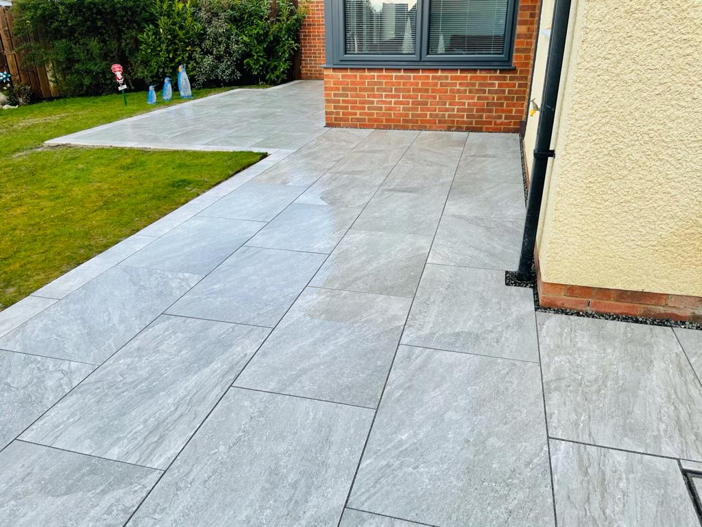 Grey porcelain paving wrapping around a house corner to a lawn edge — The Vale Company