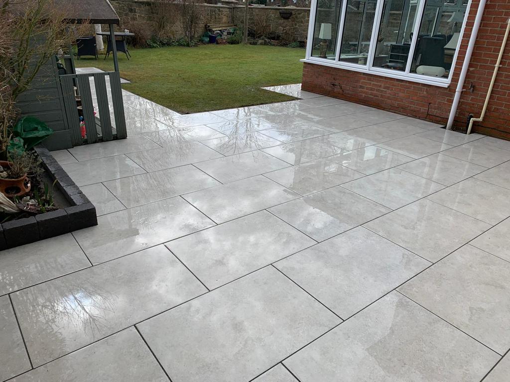 Grey porcelain patio photographed wet with charcoal block edging to a planted bed — The Vale Company