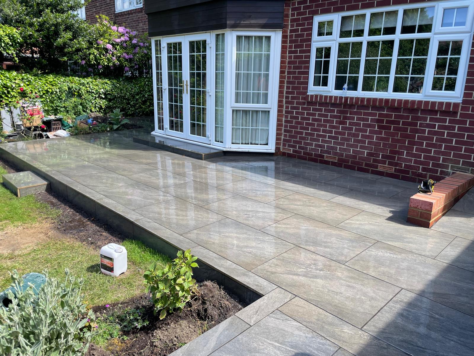Grey veined porcelain terrace with a brick plinth edge stepping down to a lawn — The Vale Company