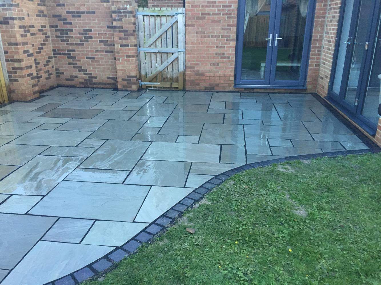 Grey Indian sandstone patio with a charcoal sett border curving against the lawn — The Vale Company