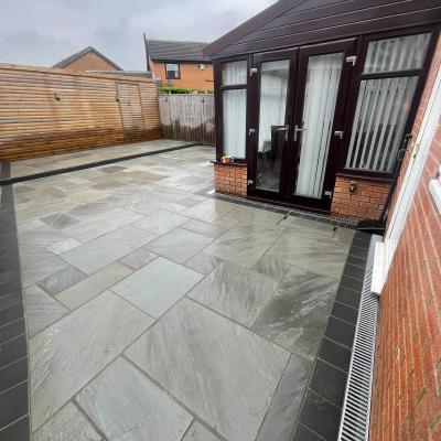 Grey sandstone patio behind a house and conservatory with a charcoal border — The Vale Company