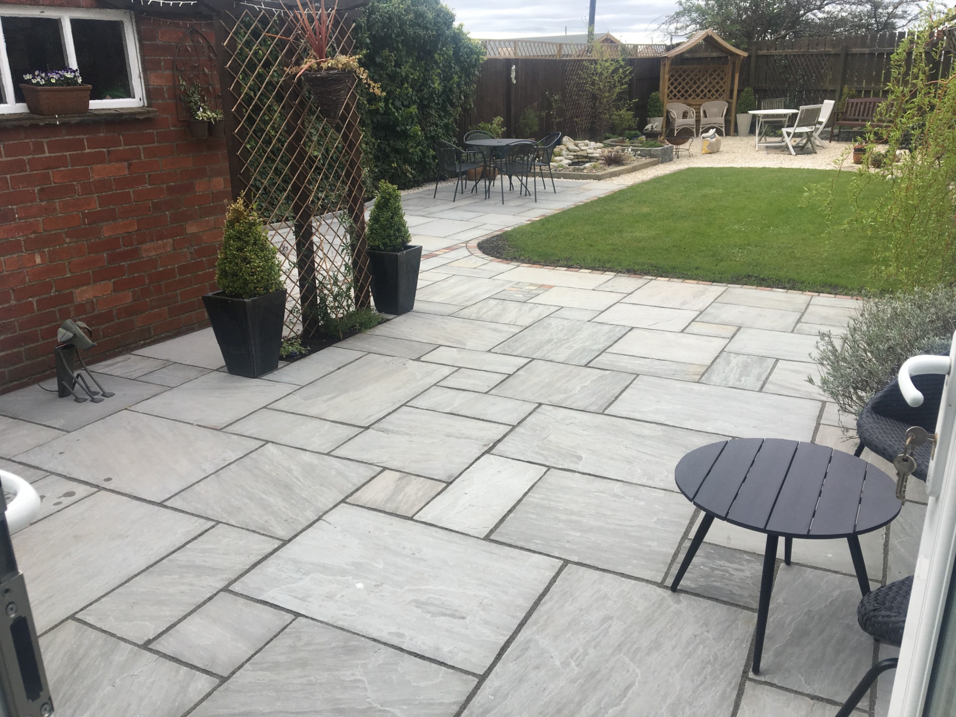 Large grey Indian sandstone terrace with a brick-edged path curving to a lawn — The Vale Company