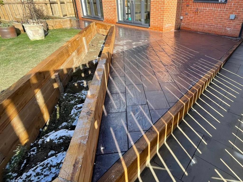 Pattern imprinted concrete terrace alongside a sleeper-retained planting bed — The Vale Company