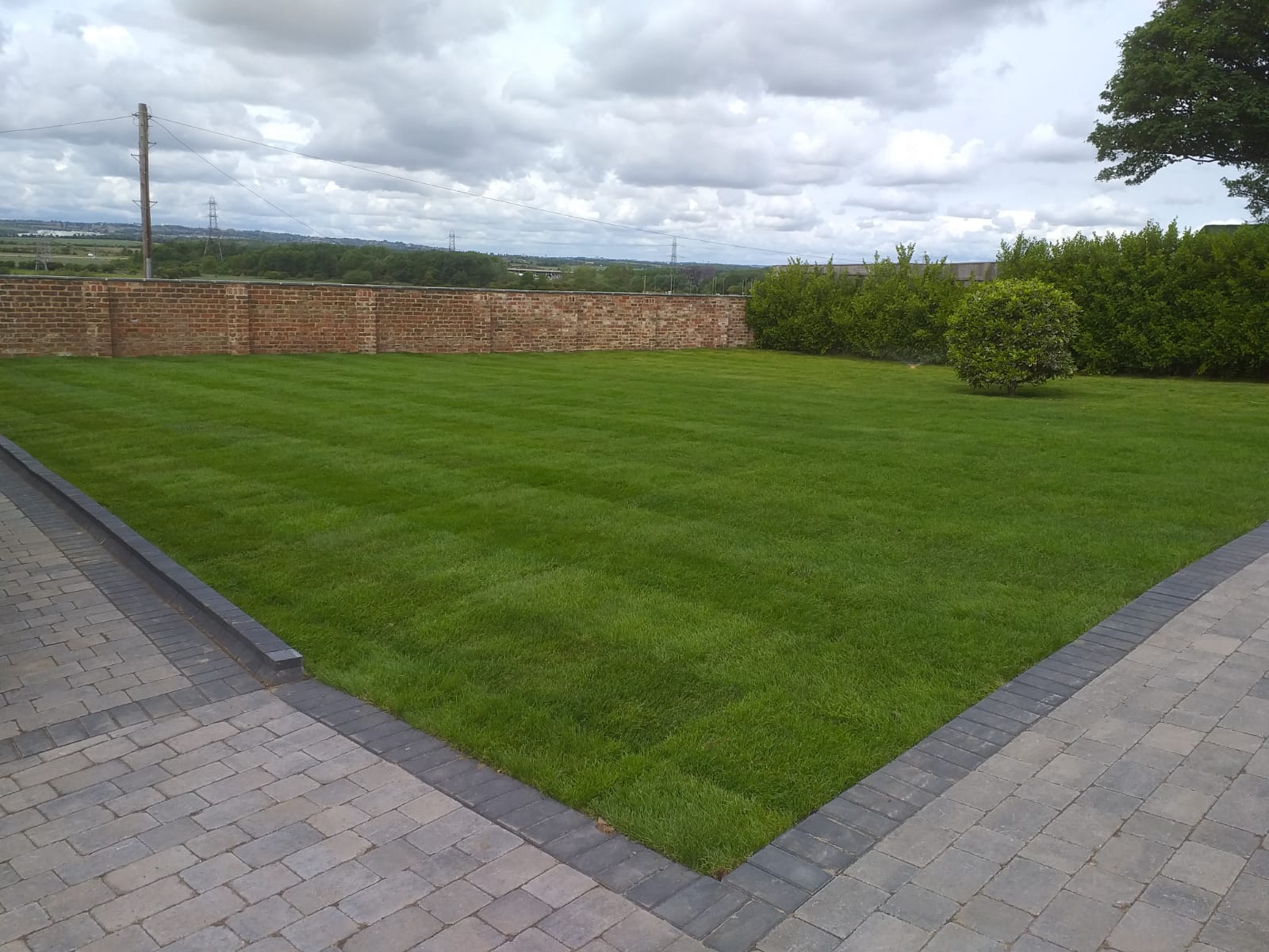 New laid turf lawn mown in stripes, meeting a block paved path with a charcoal kerb edge — The Vale Company