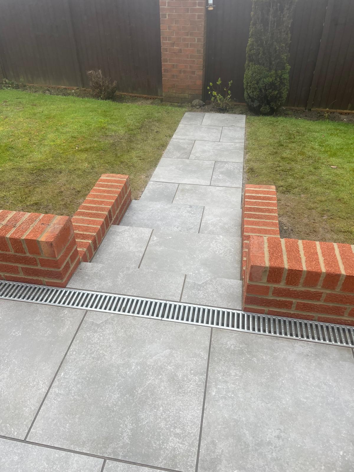 Grey porcelain path running between brick walls with a channel drain across the terrace — The Vale Company