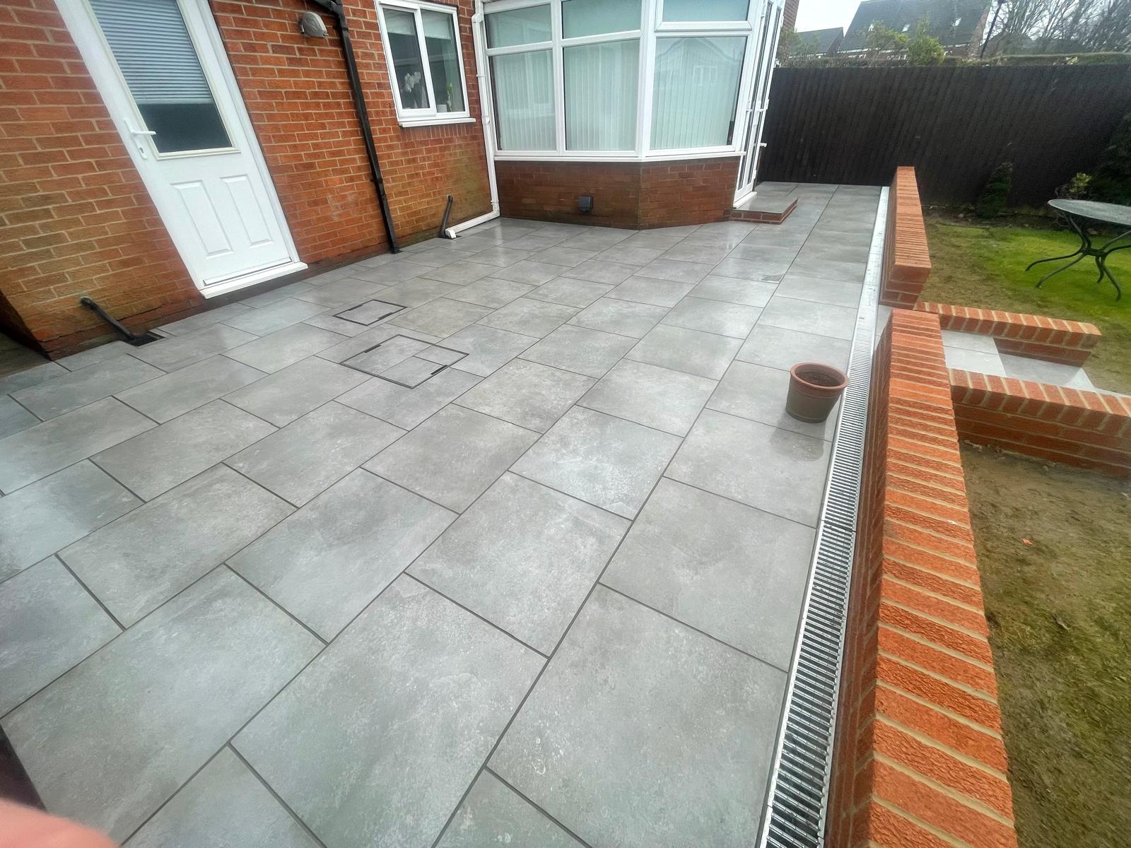 Grey porcelain terrace wrapping a house corner with two recessed covers and edge drainage — The Vale Company