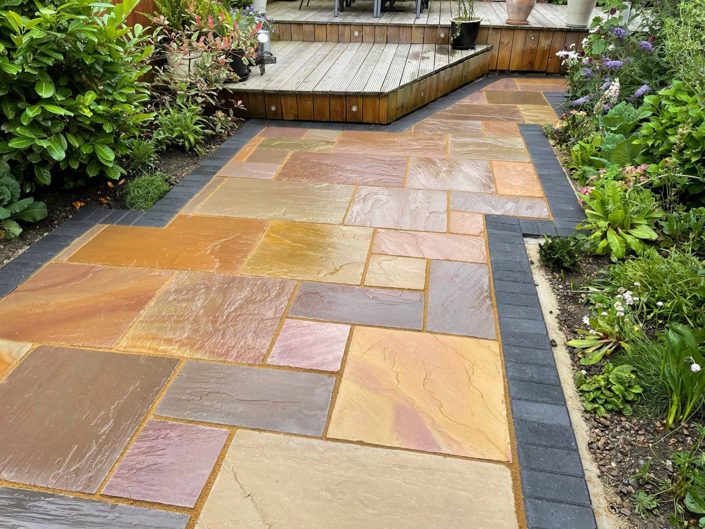 Raj sandstone path with a charcoal block border sweeping past a raised timber deck — The Vale Company