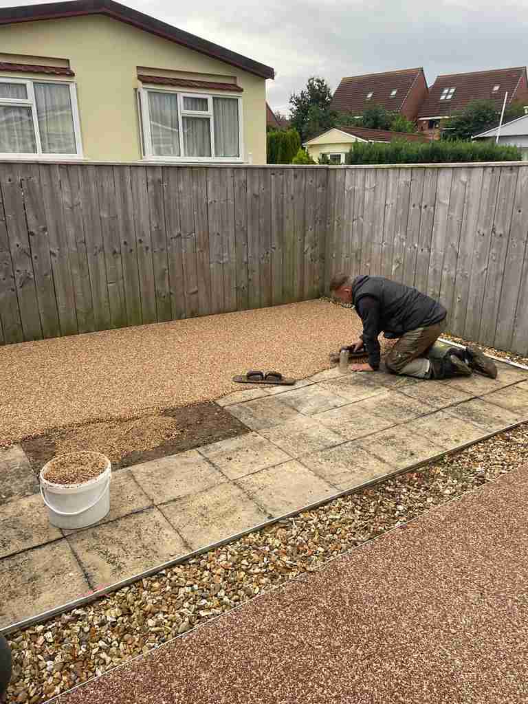 Resin bound surfacing being hand-trowelled over prepared slabs beside a gravel margin — The Vale Company