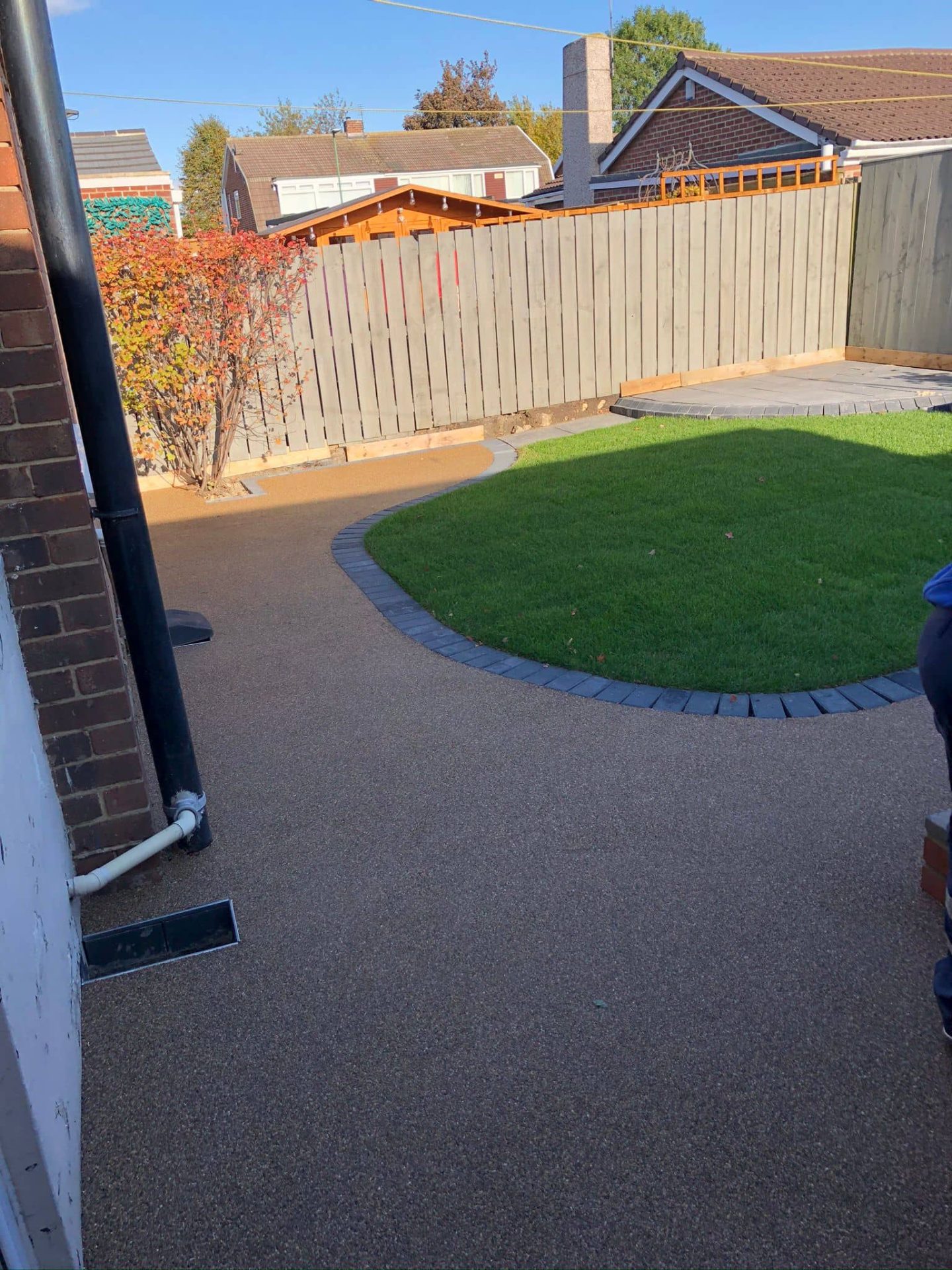 Resin bound garden path curving around a lawn held by charcoal block edging, with a channel drain at the wall — The Vale Company