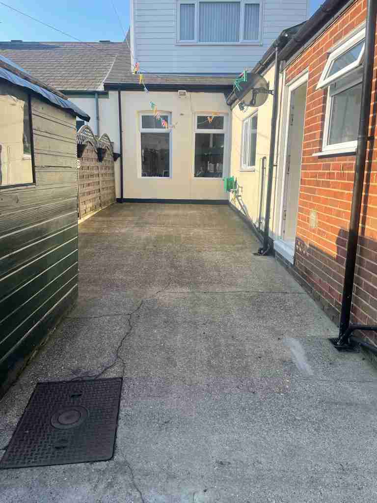 Before: cracked concrete yard with a raised inspection cover between two houses — The Vale Company