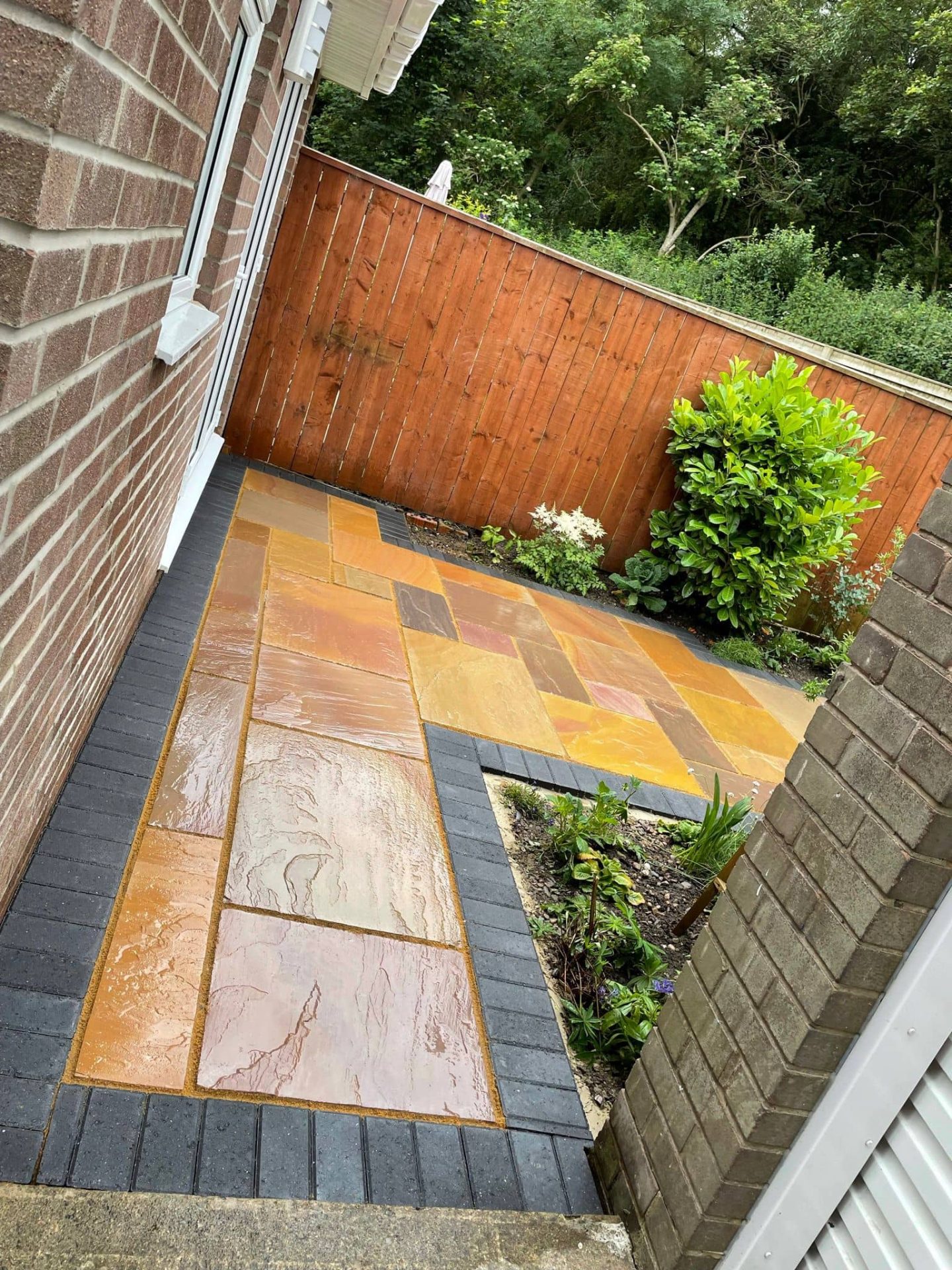 Warm multi-tone sandstone side patio with a charcoal block border and planting bed — The Vale Company