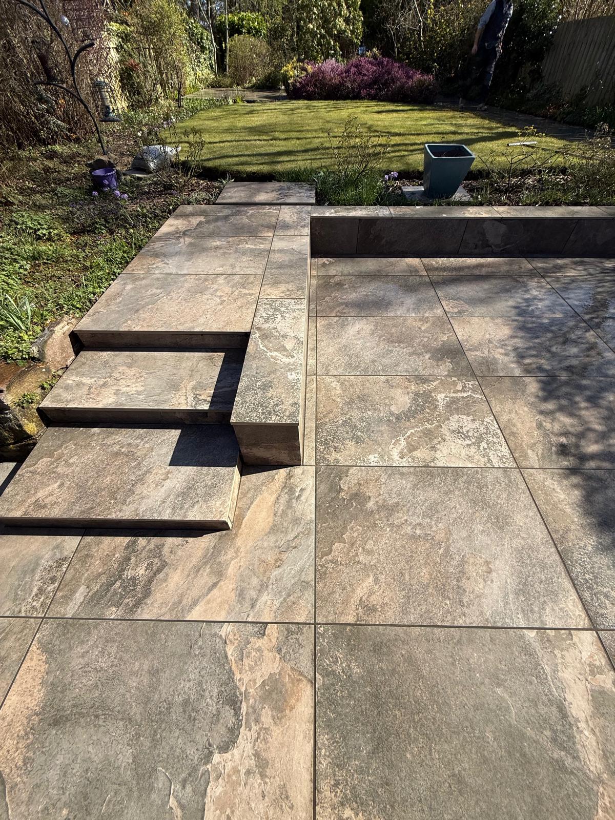 Rustic stone-effect porcelain steps and terrace edge meeting a lawn — The Vale Company