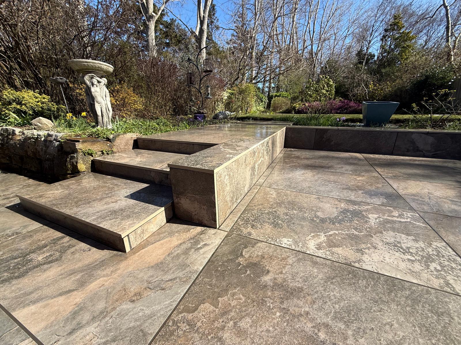 Rustic stone-effect porcelain terrace with steps and a retaining face clad in the same tile — The Vale Company