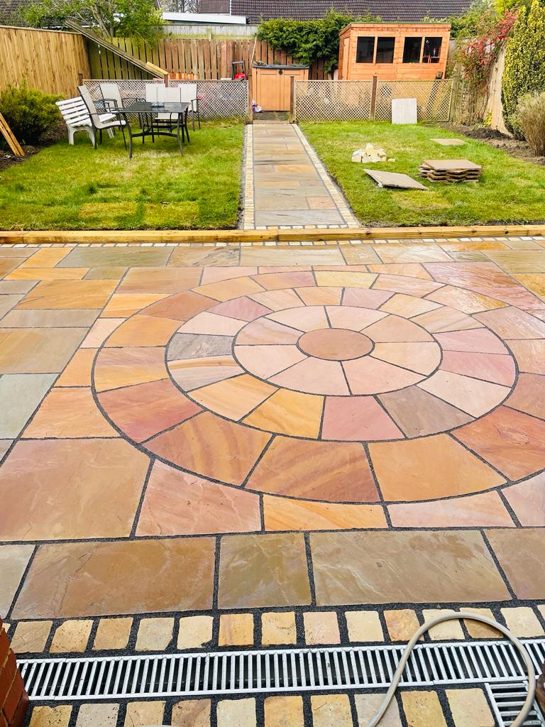 Riven sandstone patio with a full circle feature and a channel drain across the house edge — The Vale Company