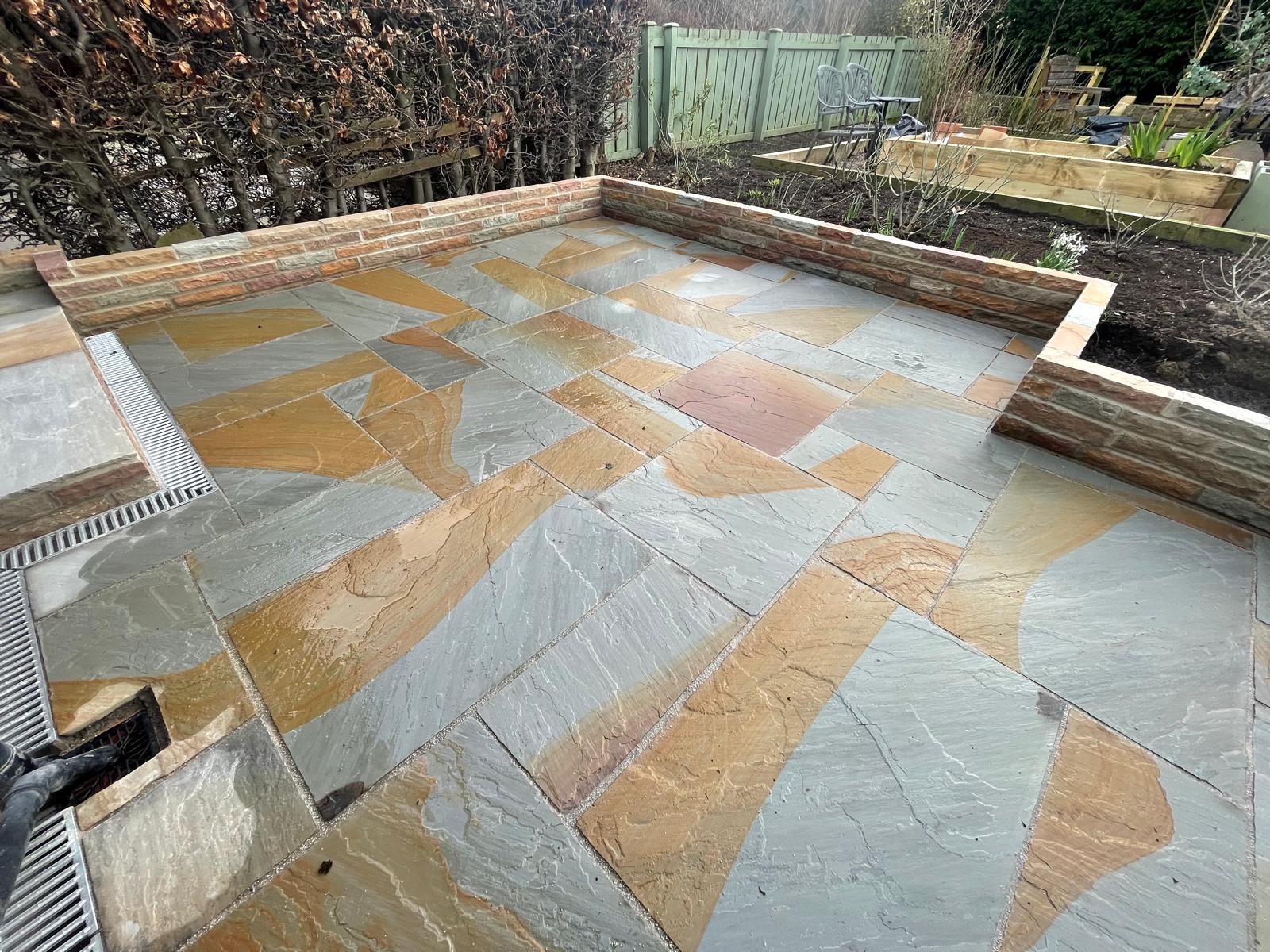 Multi-tone Indian sandstone patio enclosed by a brick retaining wall with a channel drain along the edge — The Vale Company