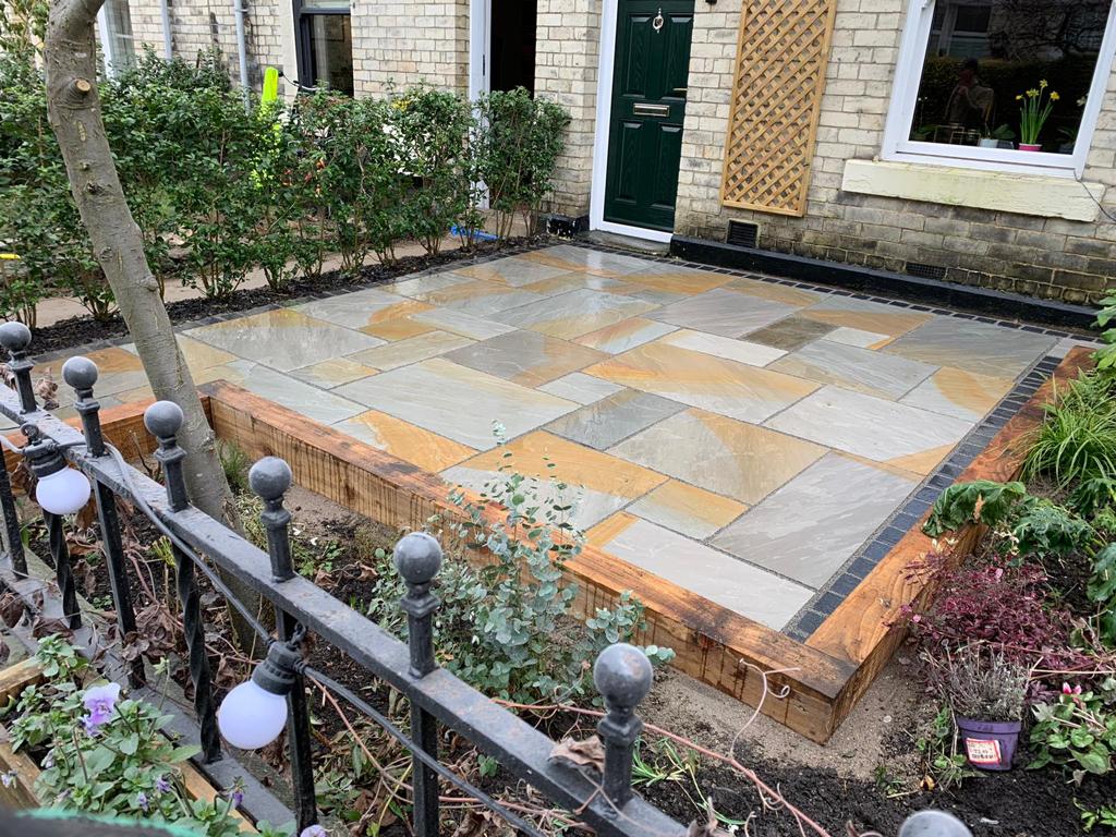 Grey and buff Indian sandstone front garden patio with a timber sleeper edge and charcoal border — The Vale Company
