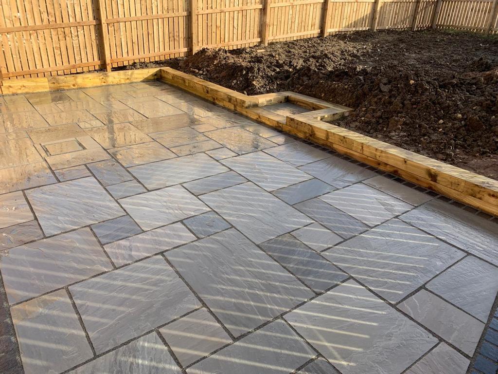 Grey Indian sandstone patio with a recessed inspection cover infilled to match and a sleeper retaining edge — The Vale Company