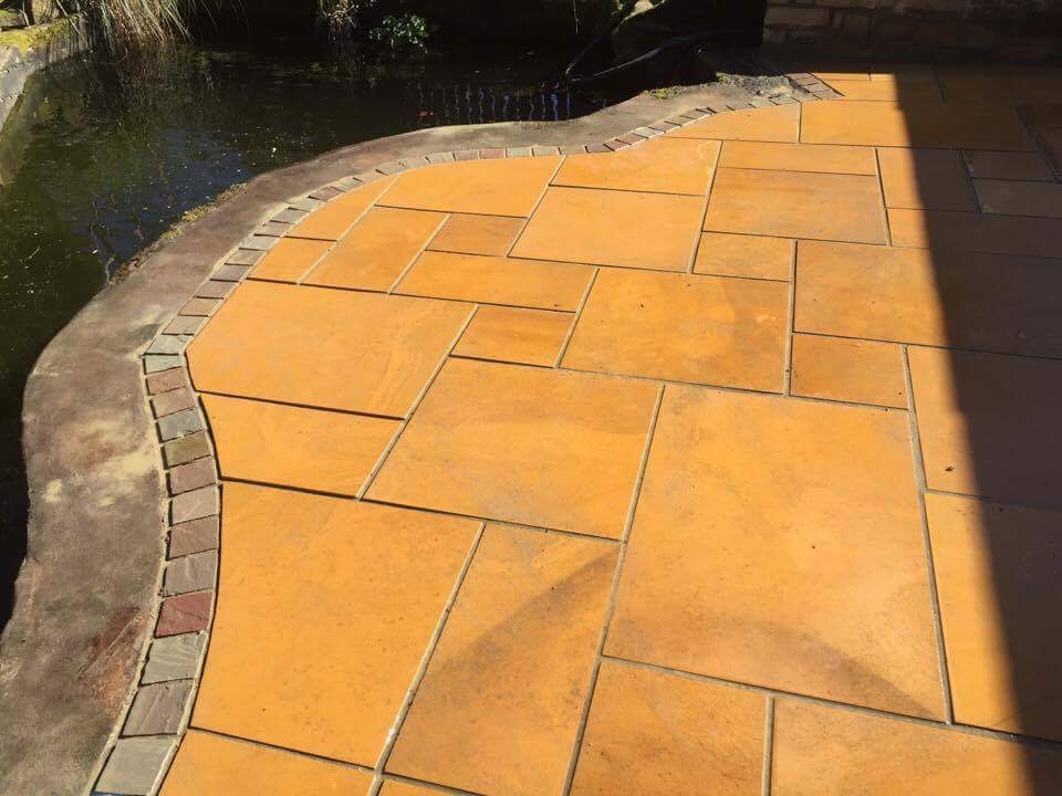 Golden Indian sandstone paving curved around a pond edge with a brick border — The Vale Company