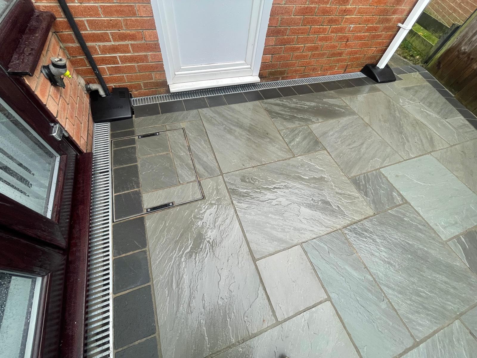 Grey sandstone doorway threshold with a charcoal border, channel drain and recessed cover — The Vale Company