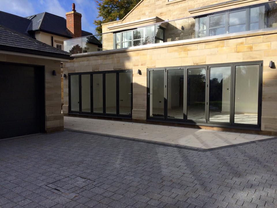 Silver granite-effect block driveway meeting an Indian sandstone patio at a stone-built house — The Vale Company