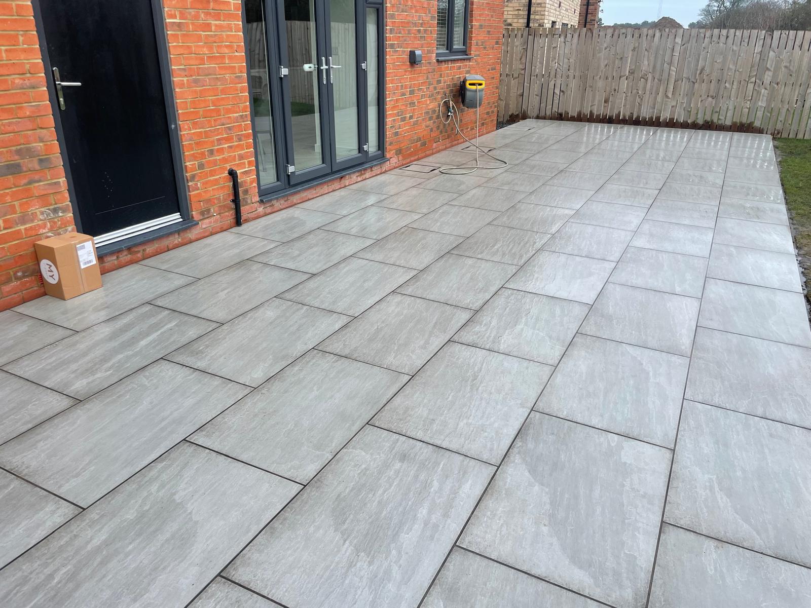 Large silver-grey porcelain terrace laid in a linear stretcher pattern across the back of a house — The Vale Company