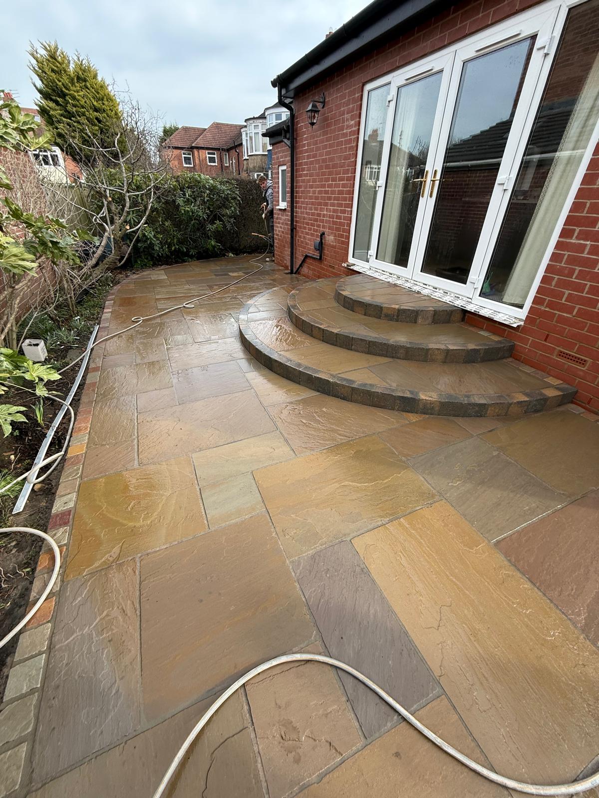 Curved sandstone steps sweeping down from patio doors onto a riven sandstone patio — The Vale Company