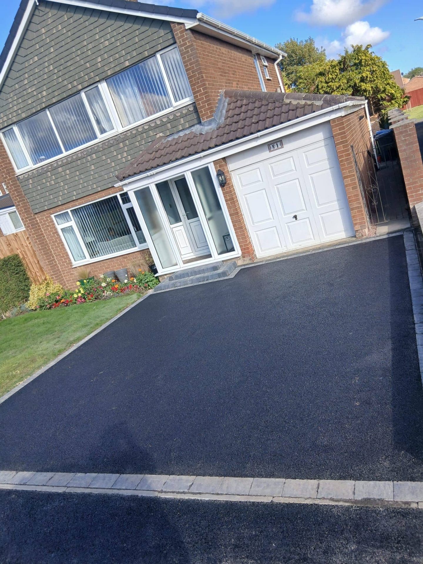 Freshly laid tarmac driveway with block paving edging running up to a garage — The Vale Company